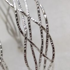 The ZusZa collection is characterized by its irregular braiding. To each wire we apply the typical surface of our workshop before welding and shaping. ZusZa is elegant and easy to wear on any occasion. We love hoops :) In our store we offer more than 100 different models. M A T E R I A L  Sterling Silver M E A S U R E M E N T S ZusZa hoops are made in 4 sizes. As each piece is completely handmade, there may be some small differences.  small: 12mm diameter, braided with 4 wires, maximum width 5mm, weight 2,3g medium: 25mm diameter,  braided with 6 wires, maximum width 10mm, weight 6,6g big: 30mm diameter,  braided with 4 wires, maximum width 6mm, weight 4,1g XL: 50mm diameter,  braided with 6 wires, maximum width 12mm, weight 8,5g F I N I S H E S Hammered Silver. Through the hammering the s Modern Twist Silver Hammered Jewelry, Elegant Braided Sterling Silver Jewelry, Modern Twist Silver Wire Wrapped Jewelry, Elegant Braided Silver Jewelry, Elegant Silver Braided Jewelry, Braided Sterling Silver Jewelry, Sterling Silver Braided Jewelry In Silver, Sterling Silver Braided Silver Jewelry, Silver Twisted Metal Jewelry