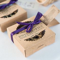 three brown boxes with purple ribbons tied around them on a table next to some cookies