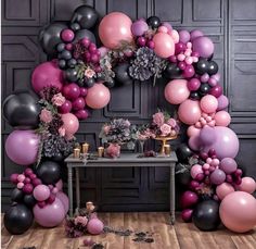 a table topped with lots of balloons next to a black and pink wall filled with flowers