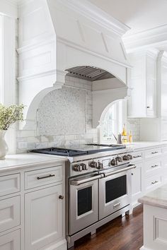 a large kitchen with white cabinets and an oven in the center, along with hardwood flooring