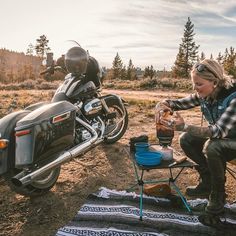 a woman sitting on a blanket next to a parked motorcycle and drinking from a cup