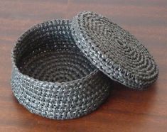 two woven baskets sitting on top of a wooden table next to each other, one is gray and the other is black