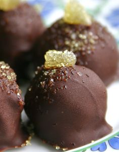 four chocolate covered desserts on a blue and white plate with gold sprinkles