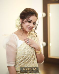 a woman in a white and gold sari posing with her hands on her chest