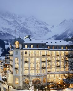 the hotel is lit up at night with snowy mountains in the background