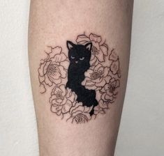 a black cat sitting in a circle of flowers on the leg with an arrow tattoo