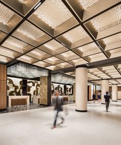 people are walking around in the lobby of a building with chandeliers hanging from the ceiling