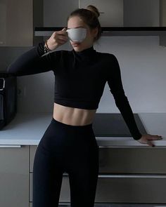 a woman in black top and leggings holding up a coffee cup to her face