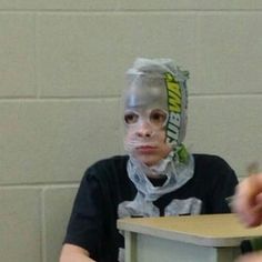 a woman with duct tape on her face sitting at a desk in front of a wall