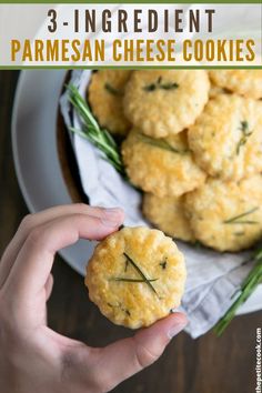 a person holding up a small biscuit in front of a bowl of rosemary sprigs