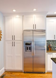 a stainless steel refrigerator in a kitchen with white cabinets and wood flooring on the side