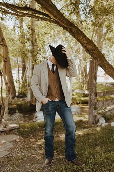 a man in a suit and tie standing under a tree with his hat up to his face