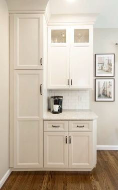 a kitchen with white cabinets and wood flooring in the middle of it, along with pictures on the wall