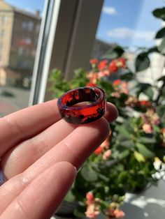 a hand holding a red glass ring in front of a window with potted plants