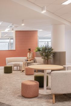 a woman sitting on a couch next to a table in an office setting with chairs and ottomans