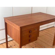 a small wooden desk with two drawers on it's sides, in front of a white wall