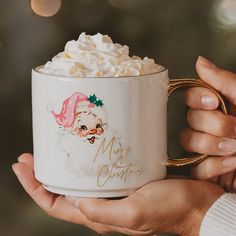 a person holding a coffee mug with whipped cream in it and a santa hat on top