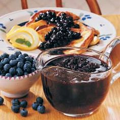 a plate with blueberries and pancakes next to a pitcher of syrup