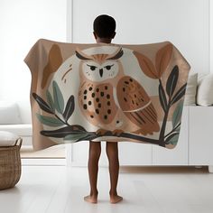 a young boy standing in front of a white wall holding an owl print blanket over his head