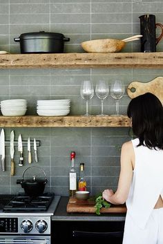 a woman standing in front of a stove top oven next to shelves filled with dishes