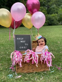 a baby in a basket with balloons and a chalkboard that says half way to one