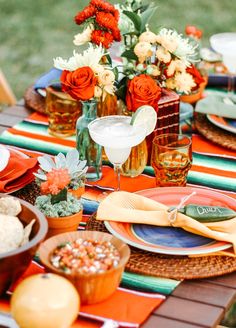 the table is set with orange and white plates, silverware, napkins, and flowers