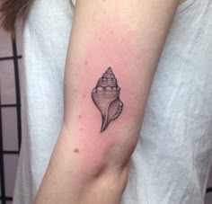 a woman's arm with a small shell tattoo on it