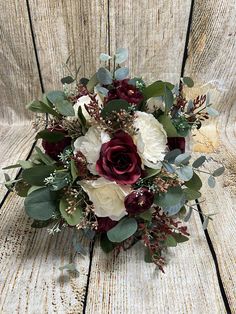 a bridal bouquet with red and white flowers sits on a wooden surface in front of a weathered wall