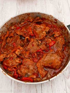 a pot filled with meat and sauce on top of a white wooden table next to a knife