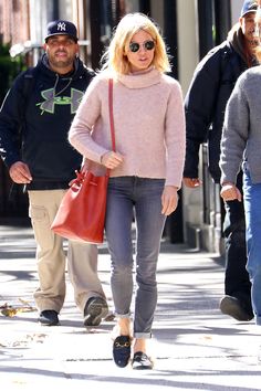 a woman in pink sweater and jeans walking down the street with two men behind her