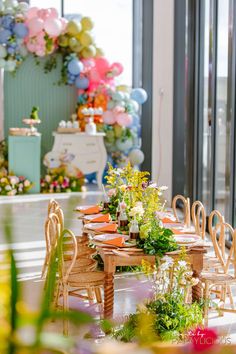 a table set up with flowers and balloons in the background