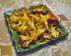 a green plate topped with cauliflower on top of a lace covered tablecloth