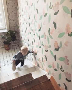 a little boy is climbing up the stairs in front of a wall with flowers painted on it