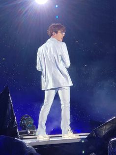 a man standing on top of a stage with his hands in his pockets and wearing white pants