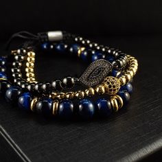 A token of French elegance, the Paris stack radiates sophistication and refinement like the city itself. The Paris stack showcases three beaded bracelets in striking blue, black and gold combo. Exquisite bracelets in this stack look perfect worn individually or stacked together for a more chic style. Indulging the adventurous spirit and wandering heart that lives within all of us, our men's bracelet stacks have been crafted to provide a touch of class to your wardrobe throughout the year. Each e Luxury Adjustable Bracelets With Black Beads, Luxury Blue Round Bead Bracelets, Elegant Blue Stackable Beaded Bracelets, Luxury Blue Beaded Bracelets, Bracelets Stack, Paris Bracelet, Bracelet Stacks, French Elegance, Blue Tigers