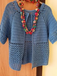 a blue crocheted sweater with beads hanging on a wooden hanger in front of a door