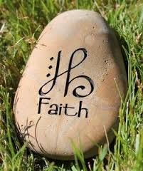 a stone with the word faith written on it sitting in the grass next to a rock