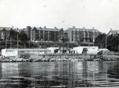 an old black and white photo of some buildings by the water in front of it