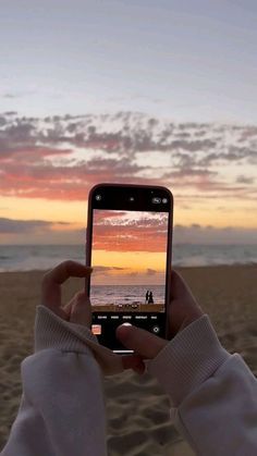 a person taking a photo with their cell phone on the beach at sunset or sunrise