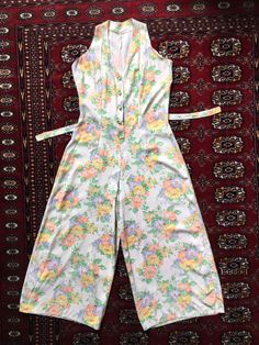 "Up for sale is this truly fantastic vintage 1940s (?) floral all-in-one sleeveless cropped wide leg jumpsuit. It features shoulder straps and a v-neck.  Fastens with three adorable plastic buttons depicting a bunch of grapes. Vertical darts at the waist and a tie belt at the back. The fabric is gentle cream soft fabric that feels like it could be rayon.  It is adorned with a striking floral and foliage pattern. With wide legs.   Please see my other listings for more vintage garments. Fabric: Printed rayon. Unlined Brand: N/A Period: This was sold to me as original 1940s but I am not 100% certain whether it is. The thread used for the seams is so brilliantly white that I can't help but wonder if it has been made more recently using vintage 1940s fabric and a vintage pattern.  Condition:  V 1940s Fabric, Sleeveless Playsuit, Combi Short, Bunch Of Grapes, Grape Bunch, Wide Legs, Wide Leg Jumpsuit, Vintage Pattern, Tie Belt