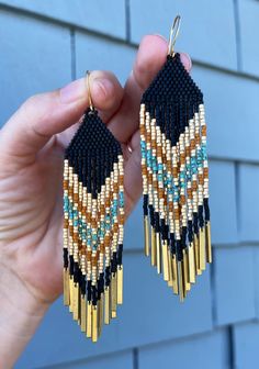 a person holding up some kind of earrings in front of a blue brick wall,