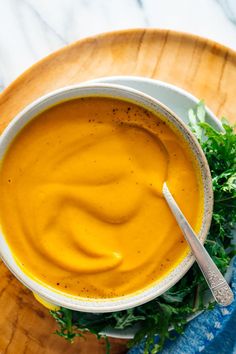 a white bowl filled with carrot soup on top of a wooden plate next to a blue napkin