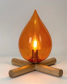 an orange glass lamp sitting on top of two wooden sticks with a light bulb in the middle