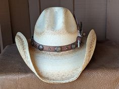 The Buffalo Run starts with a soft palm hat body that has been flame distressed so it looks like it has already been broken in. There is a wire in the brim that keeps sides in place. The brim is 4" and the crown is 5". The distressed leather hatband has replica Buffalo Nickel Conchos. The back of the band has a deer antler bead for accent. The highlight is the mature Golden Eagle feather combo. This feather is actually a trimmed turkey feather that has been hand painted to resemble an eagle feat Western Distressed Hat With Flat Brim, Rustic Distressed Adjustable Hat, Distressed Western Hat With Flat Brim, Western Distressed Flat Brim Hat, Distressed Rodeo Hat With Curved Brim, Western Distressed Curved Brim Hat, Distressed Adjustable Country Hat Band, Adjustable Distressed Hats For Country Events, Distressed Adjustable Hats For Country Events