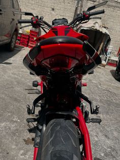 a red motorcycle parked in front of a brick wall with other vehicles behind the bike