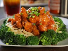 a white plate topped with broccoli covered in sauce and meat next to a drink