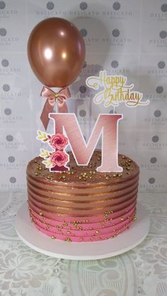 a pink and gold birthday cake with the letter m on it