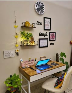 a desk with a laptop on it in front of a wall with pictures and plants