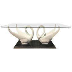 a glass table with two white swans on it's legs, sitting on a black base