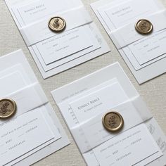 four white and gold wedding stationery cards with wax stamp on them, sitting on a table